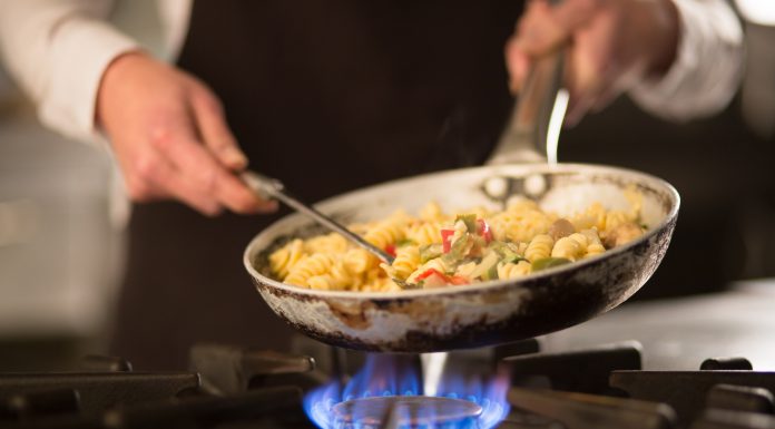 Female cook preparing pasta dish with vegetables on stove