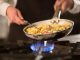 Female cook preparing pasta dish with vegetables on stove