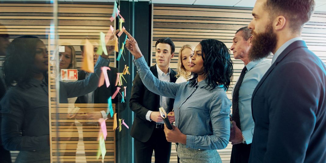 Creative group of business people brainstorming putting sticky notes on glass wall in office