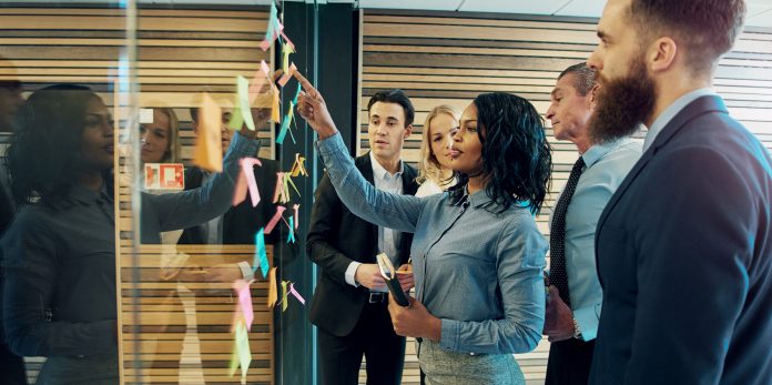 Creative group of business people brainstorming putting sticky notes on glass wall in office