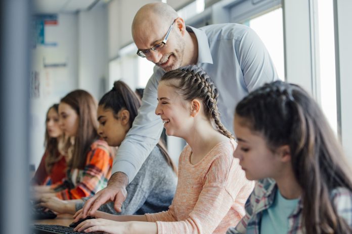 A female pupil is sitting behind a computer receiving help in lesson from a male teacher