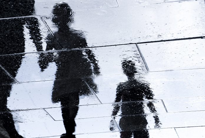 Blurry reflection shadow silhouette in a puddle of siblings and a parent walking wet city street