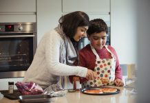A mother is helping her autistic son spread the tomato sauce over the pizza dough in preparation for dinner.