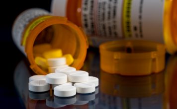 Oxycodone is the generic name for a range of opoid pain killing tablets. Prescription bottle for Oxycodone tablets and pills on glass table with reflections
