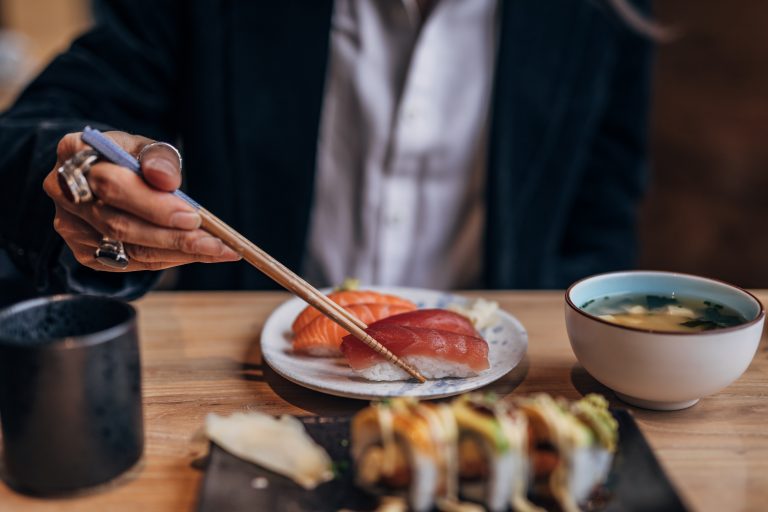 One man, gentleman sitting in restaurant alone, he is eating sushi.