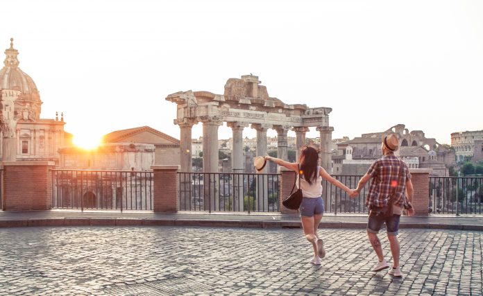 Young couple tourist walking pointing towards Roman Forum at sunrise. Historical imperial Foro Romano in Rome, Italy from panoramic point of view.