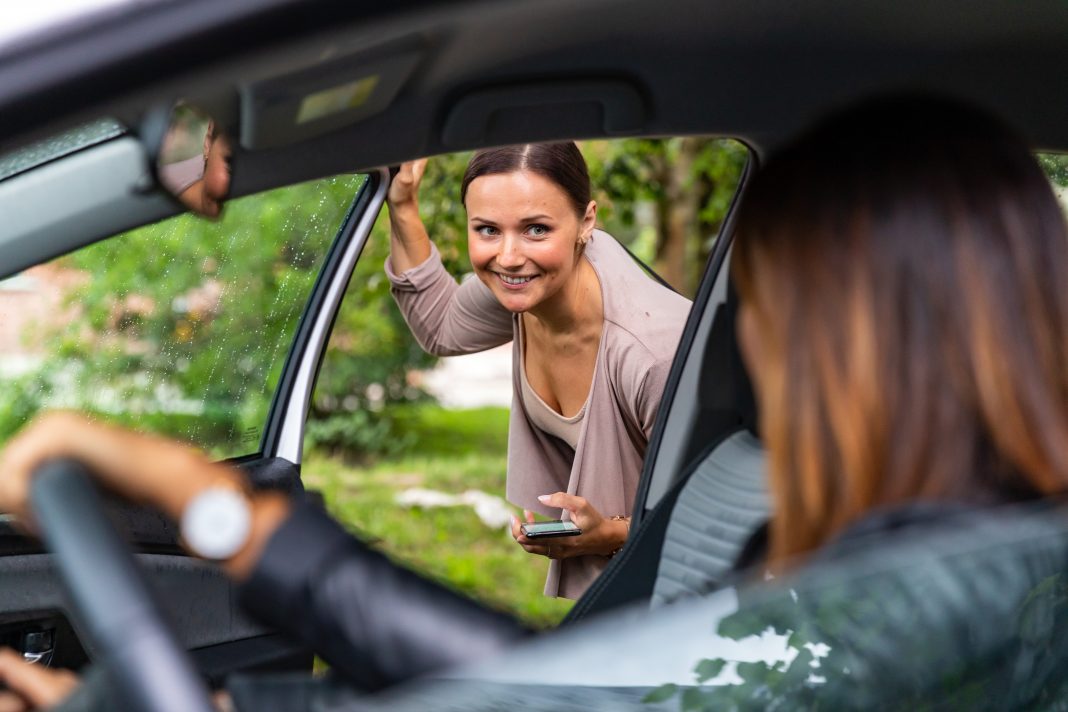 A woman is getting into a car and is looking at the driver.