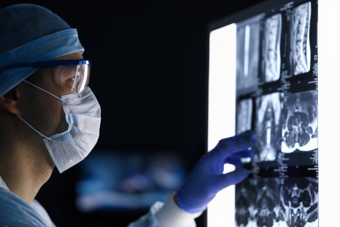 Male doctor in surgical clothes looking at vertebral mri scan headshot