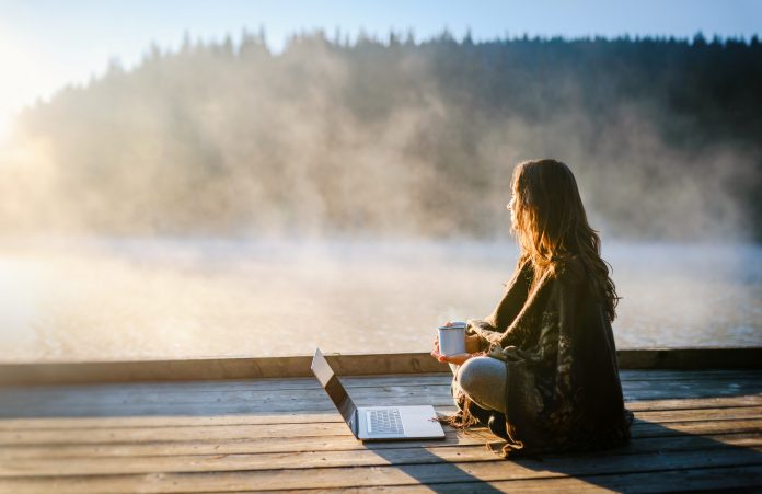 Young woman working on laptop in the nature . Leisure activities / Remote working concept.