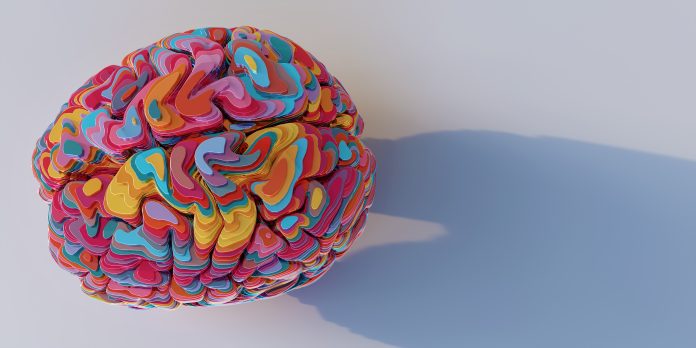 a model of a brain viewed from above, sliced into many horizontal multi-coloured layers of shiny metallic material, stacked up to form brain model. The model sits on a plain white surface with shadow, good mental health