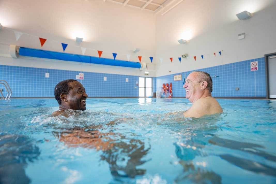 Two senior men treading water and having fun in Boldon swimming pool, North East England. They are looking at each other and laughing.