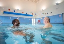 Two senior men treading water and having fun in Boldon swimming pool, North East England. They are looking at each other and laughing.