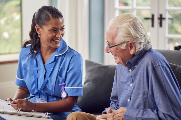 Senior Man At Home Talking To Female Nurse Or Care Worker In Uniform Making Notes In Folder, Social prescribing & building for health in the NHS