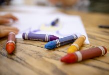 A close-up shot of colourful crayons on a wooden table with paper.