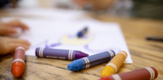 A close-up shot of colourful crayons on a wooden table with paper.
