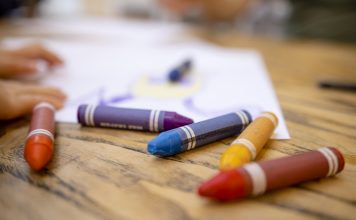 A close-up shot of colourful crayons on a wooden table with paper.