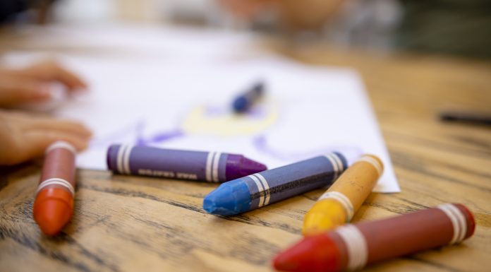 A close-up shot of colourful crayons on a wooden table with paper.