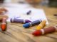 A close-up shot of colourful crayons on a wooden table with paper.