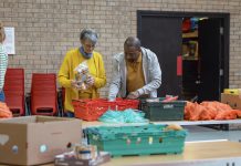 Group of volunteers organising food donations onto tables at a food bank in the North East of England. They are working together, setting up sections of the room in a church.