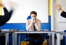 teacher looking stressed in classroom with pupils behaving badly