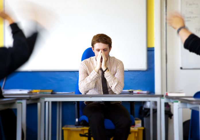 teacher looking stressed in classroom with pupils behaving badly