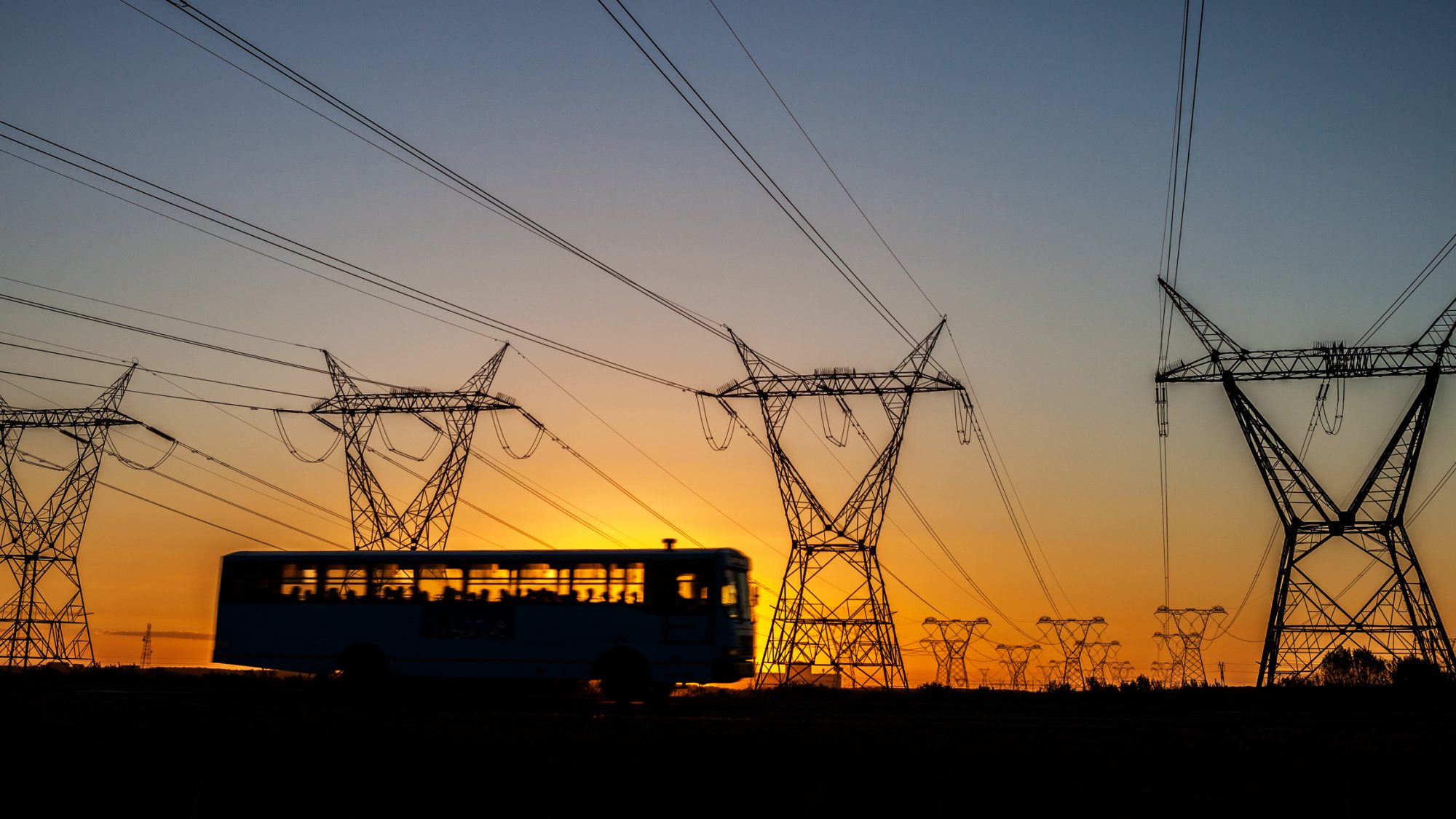 Bus with passengers driving by power lines in South Africa at sunset.