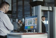 Man in uniform standing at counter at checking point and watching at monitor with x-ray of luggage