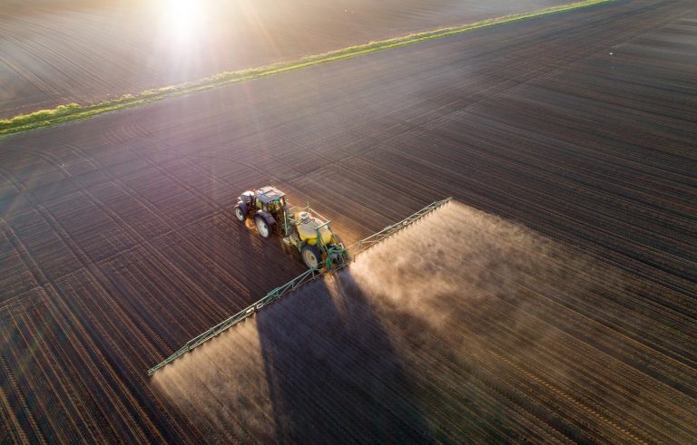 Aerial image of tractor spraying soil and young crop in springtime in field