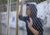 Afro-american boy behind metal fence, criminal in prison, dreaming about freedom