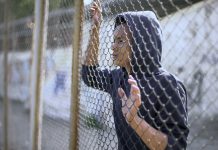 Afro-american boy behind metal fence, criminal in prison, dreaming about freedom