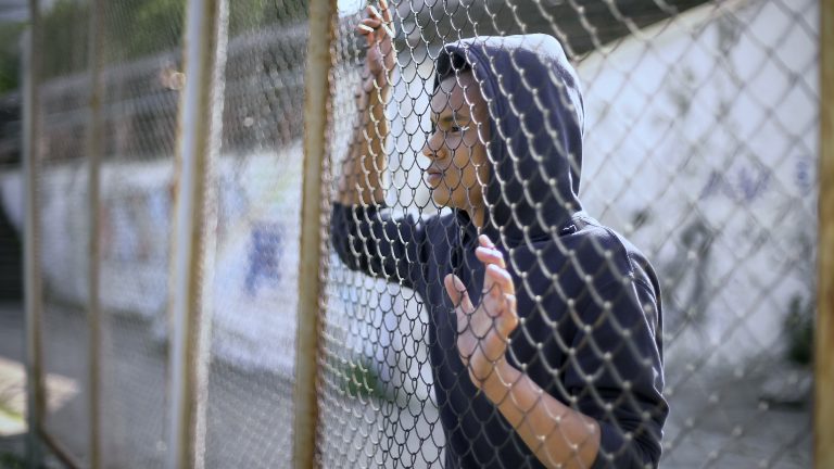 Afro-american boy behind metal fence, criminal in prison, dreaming about freedom