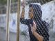 Afro-american boy behind metal fence, criminal in prison, dreaming about freedom