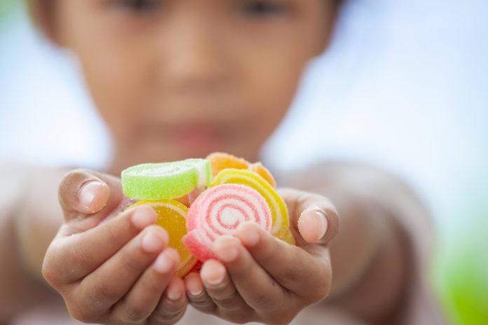 Cute asian child girl holding jelly candies in hand and sharing to other