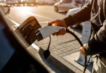 Man Holding Power Charging Cable For Electric Car In Outdoor Car Park. And heâs going to connect the car to the charging station in the parking lot near the shopping center