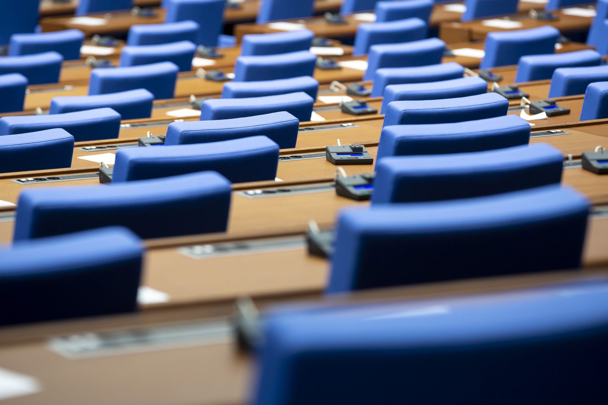 Inside of an empty parliament hall. Blue chairs in line with voting machines for every seat on the desks.