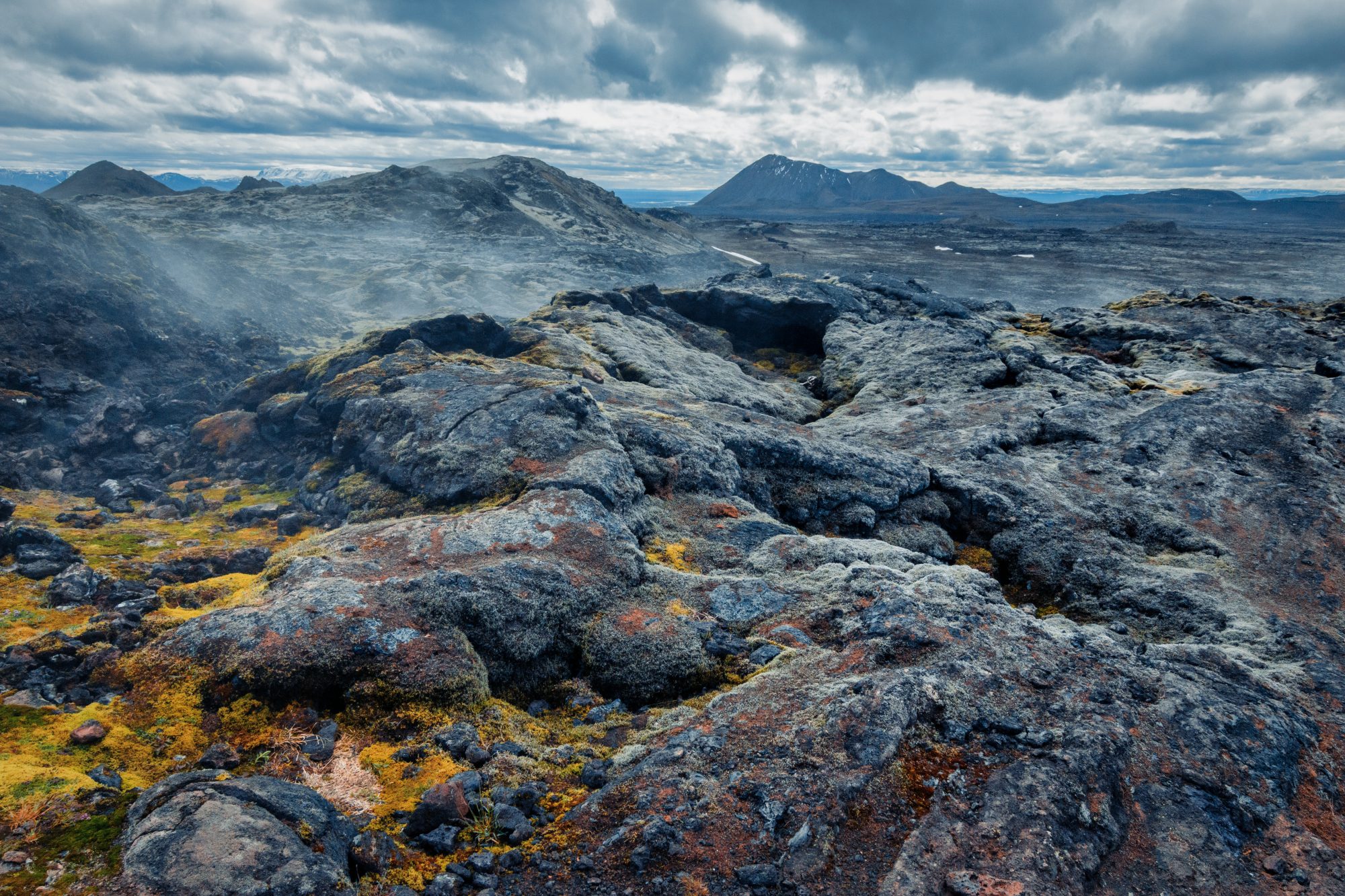 Volcanic field of rocks under storm clouds with mountains in background on Iceland