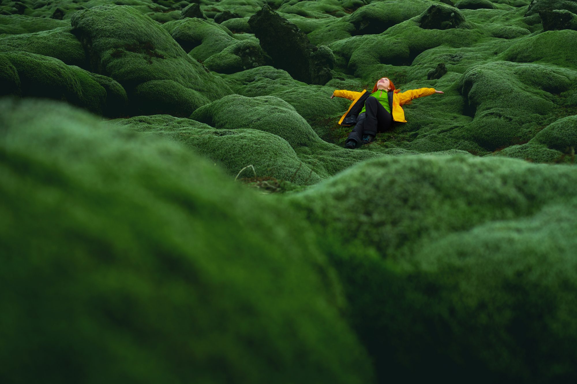 Woman posing in Icelandic moss lying on back looking up feeling happy with toothy smile