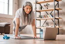 Sporty middle-aged caucasian woman standing in plank position using laptop for training at home