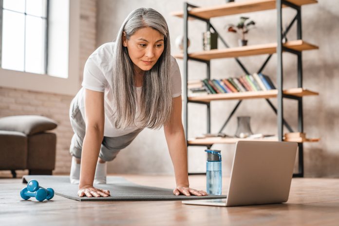 Sporty middle-aged caucasian woman standing in plank position using laptop for training at home