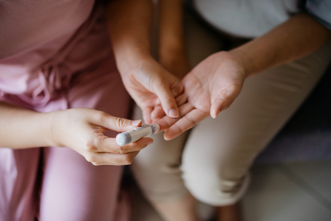 Close-up woman helping her mother check blood sugar level at home