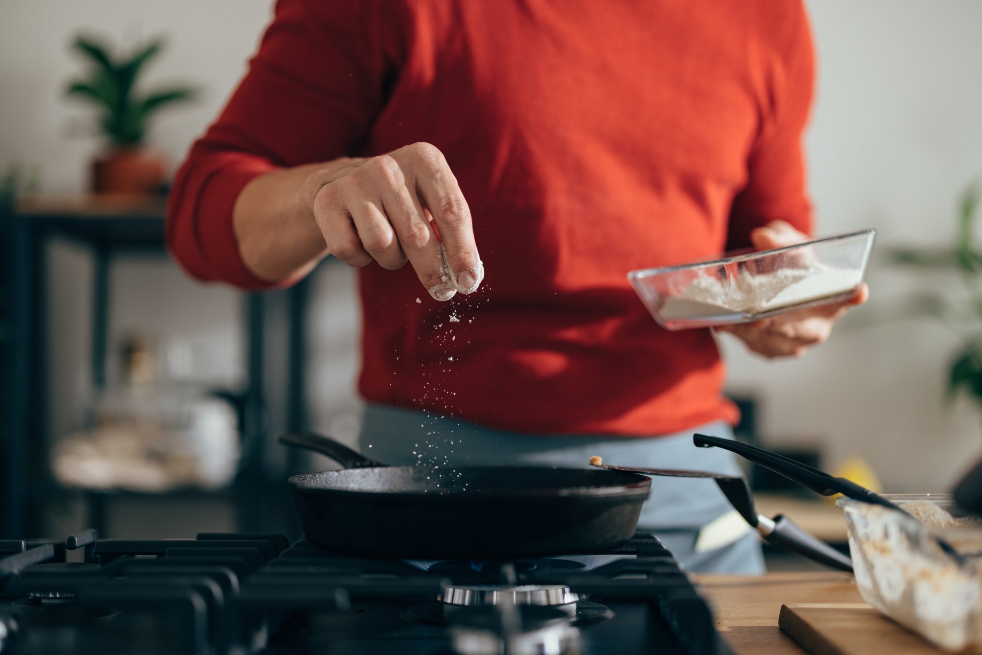 Anonymous man is preparing a meal. He is adding salt to a pan with his fingers.