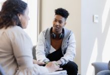 In therapy, the mid adult female counselor talks to the attentive young man and his unseen sister.