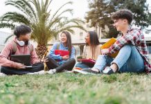 Group of multiracial international exchange university student friends sitting on the grass in the college campus