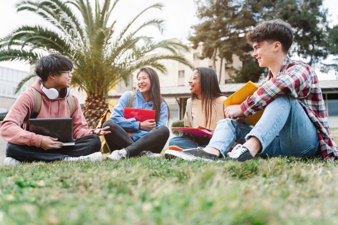 Group of multiracial international exchange university student friends sitting on the grass in the college campus