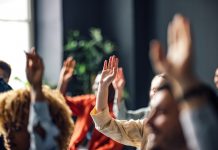 Group of people sitting on a seminar. They have their hand raised.