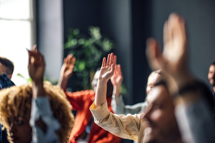 Group of people sitting on a seminar. They have their hand raised.