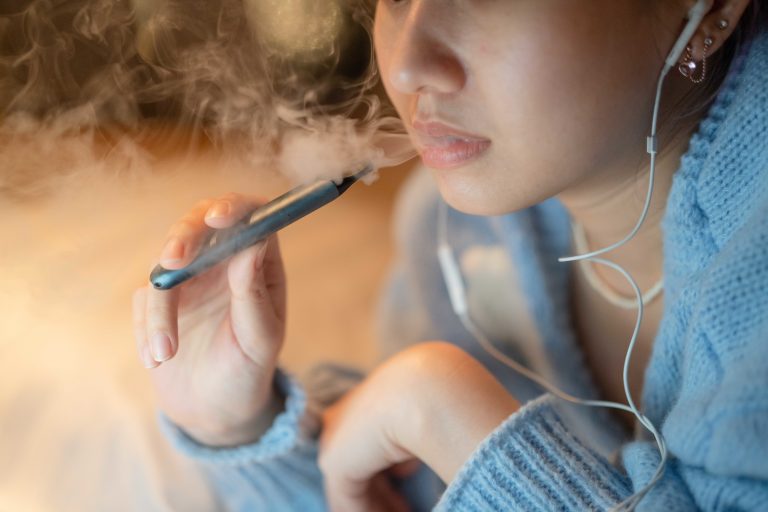 Young woman vaping an electronic cigarette for relax while working at night