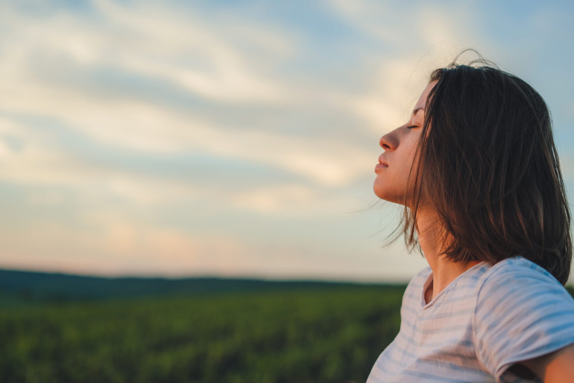 Profile view calm woman breathing fresh air and dreaming with eyes closed, standing int the cornfield. Wellbeing concept. Summer vacation. Harmony concept. Fresh air.