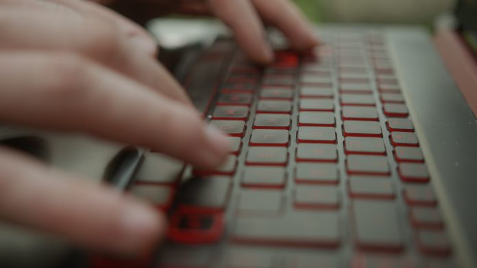 Close-Up of Laptop Keyboard and Hands Typing by Young Man
