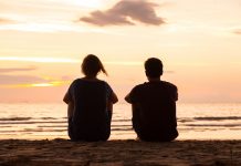 Friends sitting together on the beach and watching sunset, friendship concept